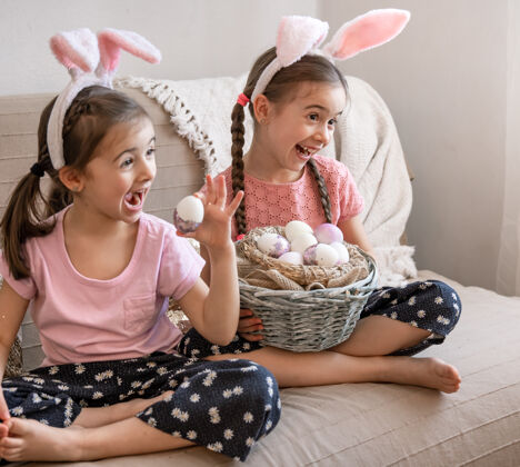 复活节有着兔子耳朵的快乐小姐妹们拿着一篮子复活节彩蛋摆姿势孩子们兔子女孩