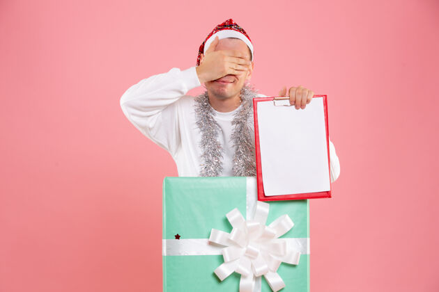 礼物正面图：年轻男性在粉红色背景下手持文件笔记睡衣圣诞便条