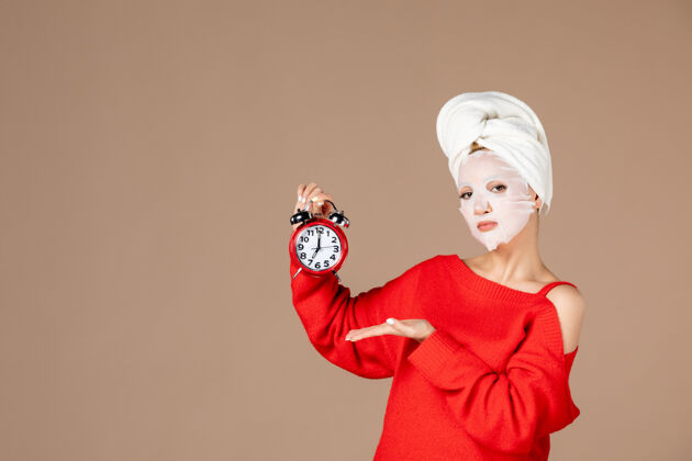 淋浴正面图：戴着面具的年轻女性 手持粉色背景上的时钟肖像美女年轻女性