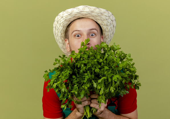 制服令人印象深刻的年轻英俊的斯拉夫园丁在制服和帽子举行香菜从后面它隔离在橄榄绿的墙上斯拉夫花园香菜