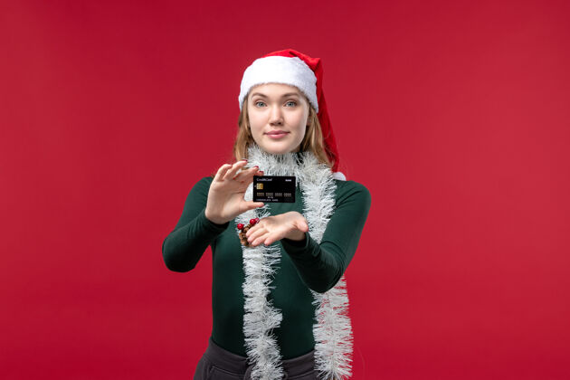 漂亮的女性正面图漂亮的女人拿着红色背景的黑色银行卡肖像卡片圣诞节