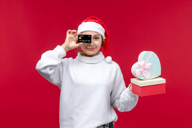 欢乐正面图红色背景上的年轻女性 带着银行卡和礼物成人银行圣诞节
