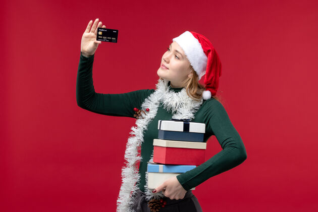 圣诞节正面图：手持礼物和红色背景的银行卡的年轻女子红色银行卡片