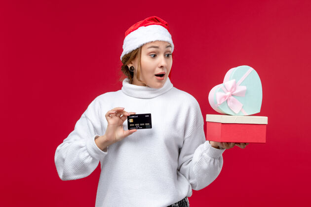 年轻女子正面是一位年轻女士 她拿着礼物和红色背景上的银行卡圣诞礼物正面