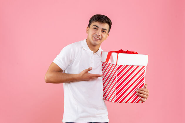 自信正面是年轻男性 粉色背景上有一份圣诞礼物礼物微笑年轻男性