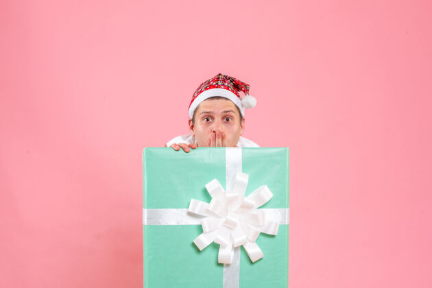睡衣正面图：身穿白色衬衫的年轻男性 粉色背景上的礼物圣诞节正面盒子