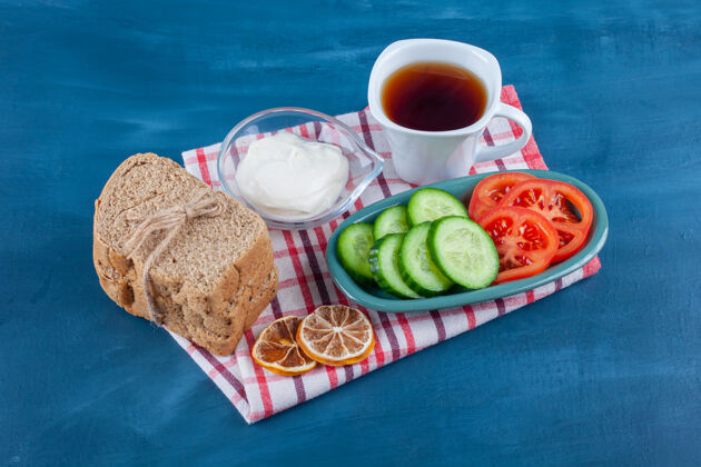 面包清淡的早餐一杯茶 一碗黄瓜片和西红柿 面包放在蓝色的茶巾上茶茶巾风味
