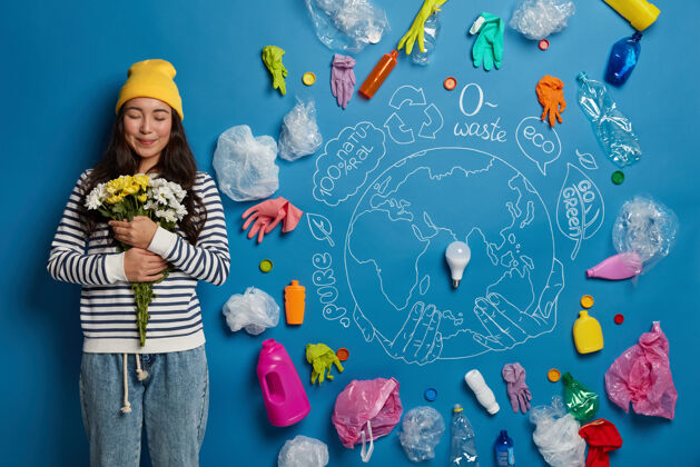 欢呼高兴的韩国妇女满意地得到了花束 手持白色和黄色的花 站在蓝色墙上画的星球和塑料垃圾周围 清洁大自然的污染韩国再利用塑料