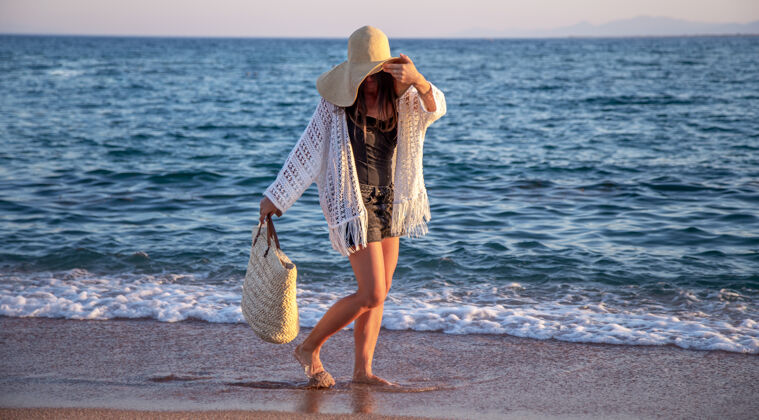 曲线一个戴着大帽子 挎着柳条袋的女孩走在海边暑假的概念夏天大海帽子