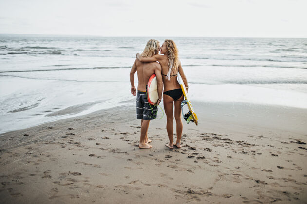 爱照片中的男子和女子在游泳衣举行冲浪板对海微笑女性男性
