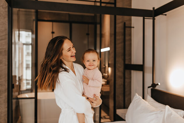 女儿穿着浴衣的女人抱着微笑的小孩子卧室里母亲和女儿的画像卧室公寓长袍