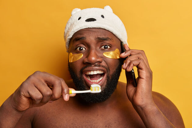 新鲜有趣的黑人男人关心牙齿 拿着牙膏的牙刷 戴着减少细纹的胶原蛋白贴片说话人快乐