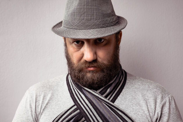 背景特写一个留胡子的男人穿着浅灰色的t恤 帽子和围巾在灰色的背景成人白种人服装