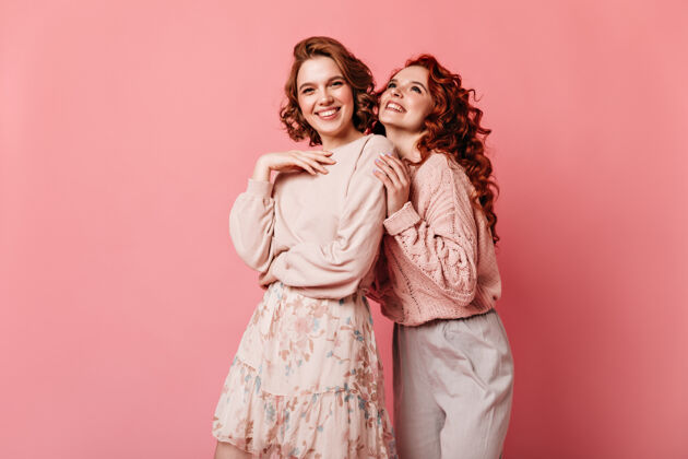 两个人快乐的女孩在粉红色的背景上表达快乐两位穿着考究的女士对着镜头微笑的前视图在一起孤立的粉色情绪