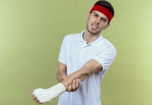 手戴着头巾的年轻运动型男子抚摸着他缠着绷带的手 感到绿色的疼痛绷带运动年轻