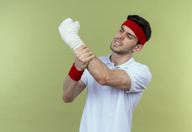 年轻戴着头巾的年轻运动型男子抚摸着他缠着绷带的手 感到绿色的疼痛绿色绷带运动