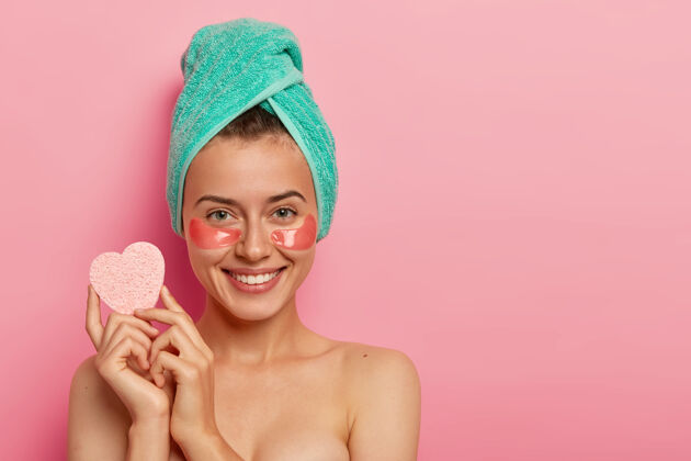 欧式年轻快乐的女人戴着胶原蛋白补水贴在眼睛下面 拿着海绵卸妆 做美容 淋浴后皮肤清新乐观水疗快乐