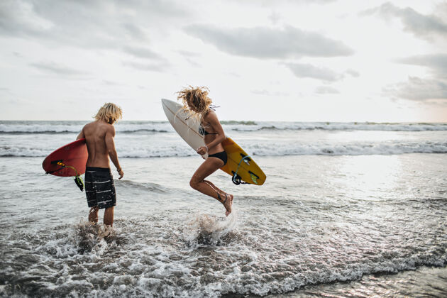 海洋苗条的男孩和女孩跳进海水里拿着冲浪板男人男人海洋