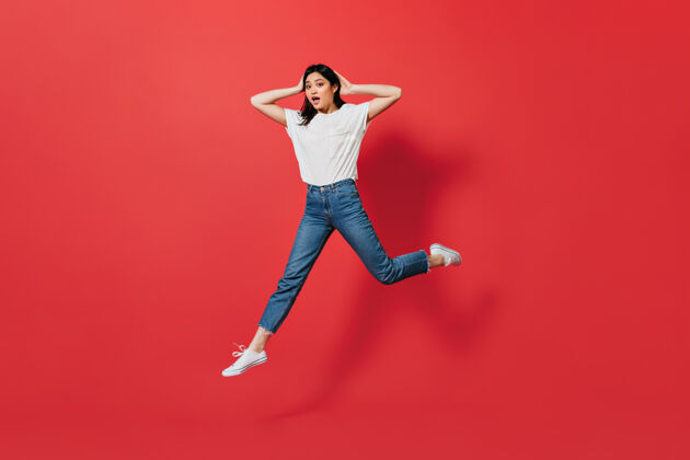 情感情绪化的亚洲女人穿着牛仔裤跳红墙欢呼兴奋跳跃