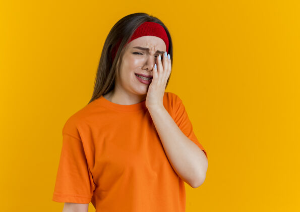 戴一个戴着头带和腕带 手放在脸上的年轻运动型女人头带橙色腕带