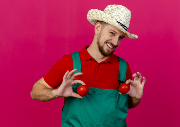 近面带微笑的年轻英俊的斯拉夫园丁 身着制服 戴着帽子 胸前抱着西红柿花园男人微笑