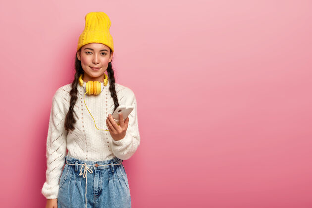 小玩意可爱的东方少女用耳机连接手机 听音乐年轻人应用程序毛衣