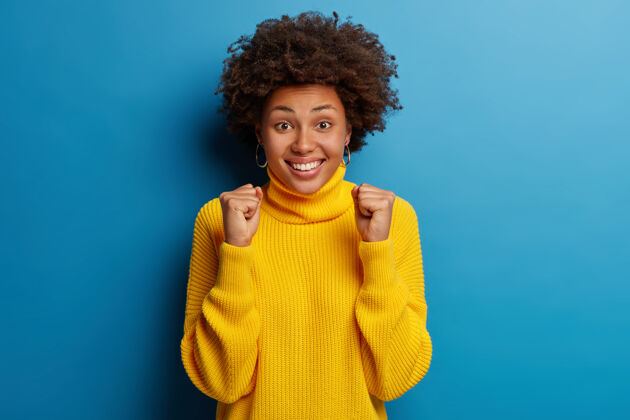 年轻积极的美国黑人年轻女子笑容满面 身穿黄色套头衫 背景为蓝色服装人类积极