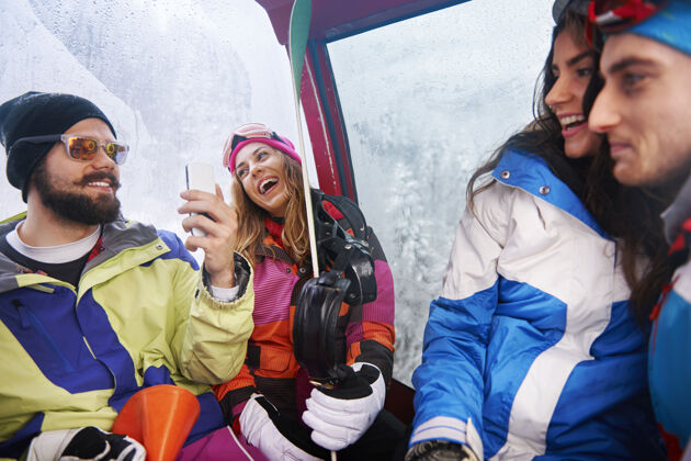 雪两对情侣在玩滑雪坐着笑摄影师