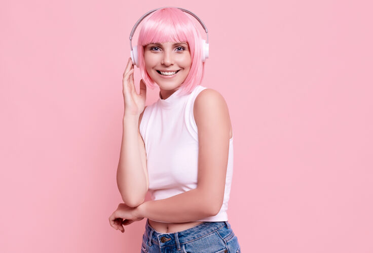 美丽粉红头发的美女肖像在耳机里欣赏音乐无线女性模特