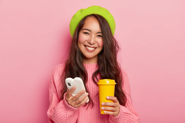 饮料可爱快乐的女人 表情愉快 用手机上网聊天 拿着黄色的咖啡外卖杯通信休闲科技