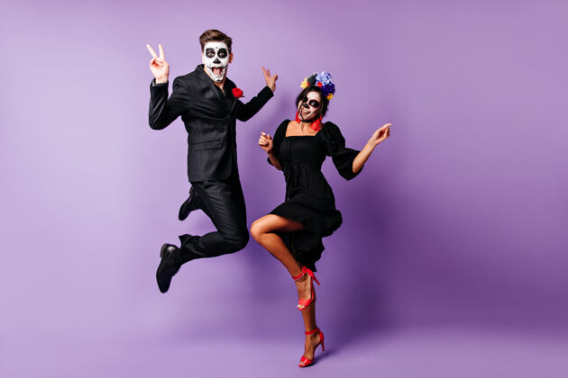僵尸一对穿着僵尸服装在紫色背景上跳舞的欧洲夫妇的完整肖像有趣的年轻人在万圣节活动中鬼混文化骷髅服装