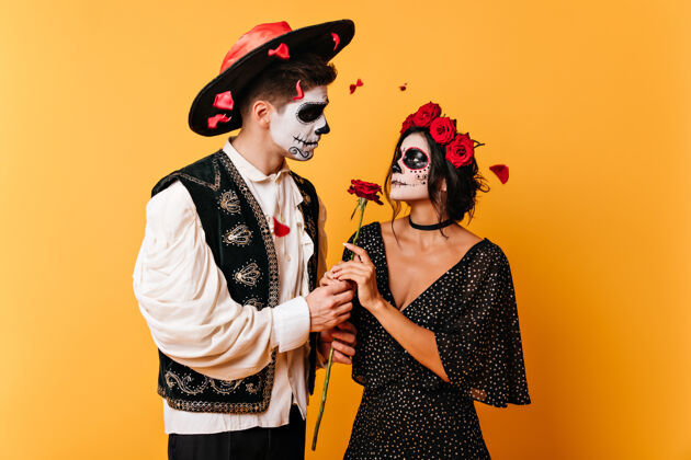 恐怖一对相爱的情侣抱着玫瑰的照片有着艺术脸谱的男人和女人温柔地看着对方的眼睛服装死亡文化