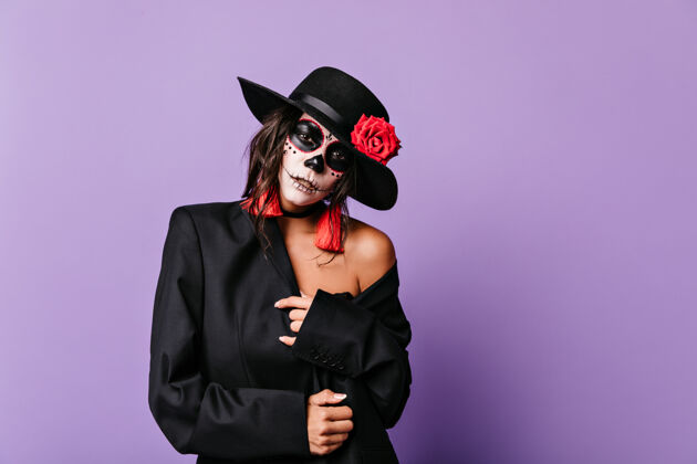 僵尸一个充满激情的女人的特写肖像戴着黑色帽子的模特在淡紫色的墙上摆着姿势恐怖拉丁语玫瑰