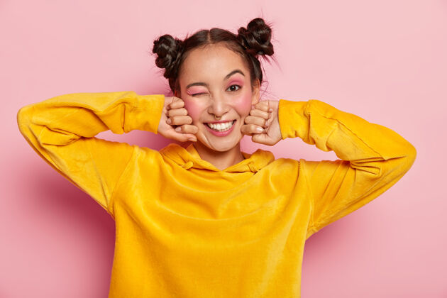 运动衫可爱的亚洲年轻女子 一脸幸福的表情 眨着眼睛积极的微笑 在室内玩得很开心 两个发结微笑胭脂休闲