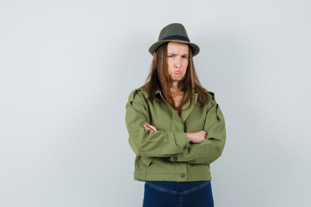 休闲年轻的女性交叉双臂站在夹克 裤子 帽子和看起来冒犯 正面视图站立女人青春
