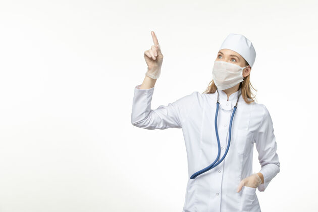 冠状病毒防护前视图：穿着白色医疗服 戴着口罩的女医生在白墙上抵御冠状病毒的传染疾病大流行冠状病毒