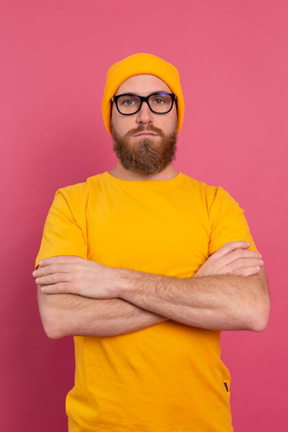 时尚时尚帅气的留着胡子的欧洲男人的肖像 穿着休闲的黄色衬衫 戴着粉色背景的帽子和眼镜眼镜眼镜欢呼