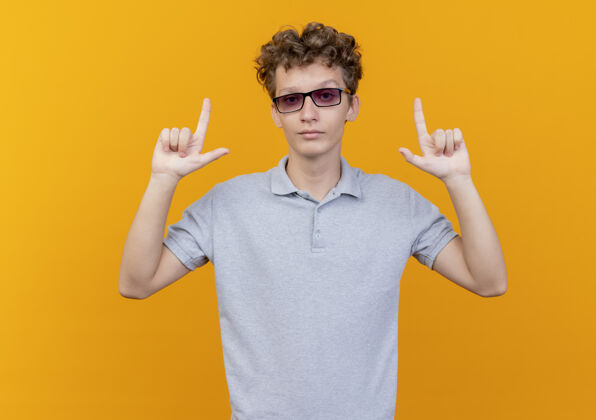 男人一个戴着黑眼镜的年轻人 穿着灰色马球衫 一张严肃的怀疑的脸 用手指指着橙色的墙上马球眼镜严肃