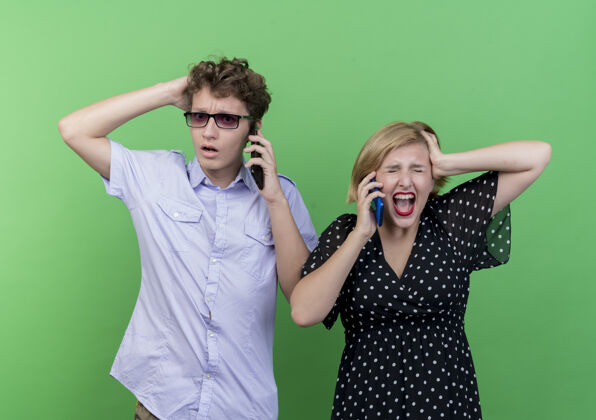 女人一对年轻漂亮的夫妇站在绿色的墙上 愤怒的男人和女人在用手机交谈手机男人生气