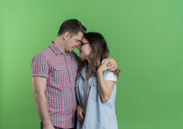 男人一对穿着休闲服的年轻男女站在一起 在绿色的墙上拥抱着幸福的爱情拥抱站着衣服