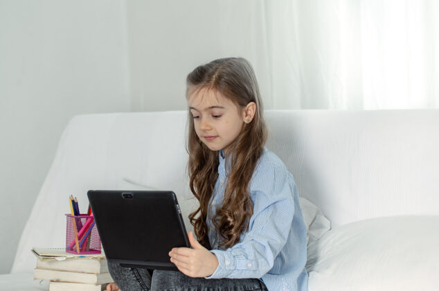 小学一个小学女生坐在家里的沙发上 带着一台笔记本电脑在网上上课 因为冠状病毒大流行而导致隔离远程女学生孩子