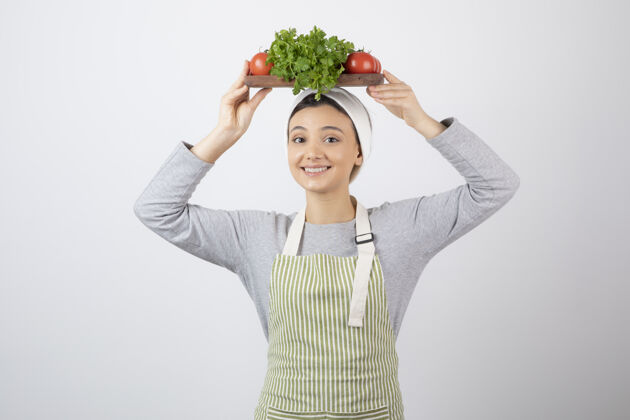 人微笑可爱的女模特头上拿着一块新鲜蔬菜的木板拿着微笑板