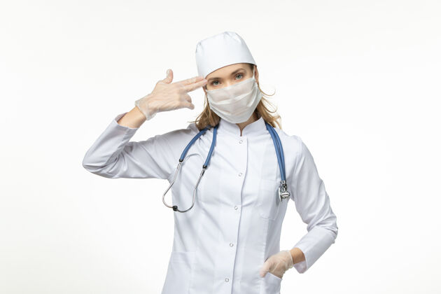 专业人员正面图女医生穿着医疗服戴着口罩和手套因白色办公桌上冠状病毒大流行冠状病毒病手套病毒面罩