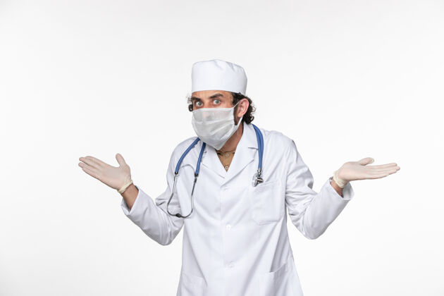 正面正面图男医生穿着医疗服 戴着无菌口罩 以防白色地板上的冠状病毒冠状病毒大流行疾病实验室外套套装疾病