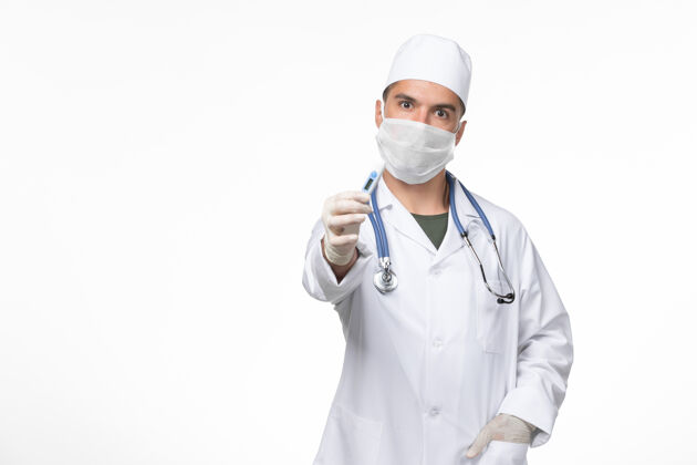 套装正面图男医生穿着防毒服和口罩手持防冠状病毒装置上的白墙病毒-疾病大流行疾病听诊器视图