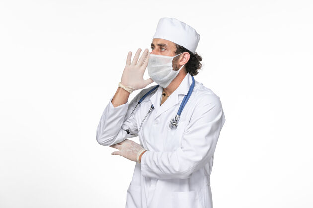 医疗正面图男医生穿着医疗服 戴着无菌口罩 以防冠状病毒引起白墙飞溅病毒大流行正面防护大流行