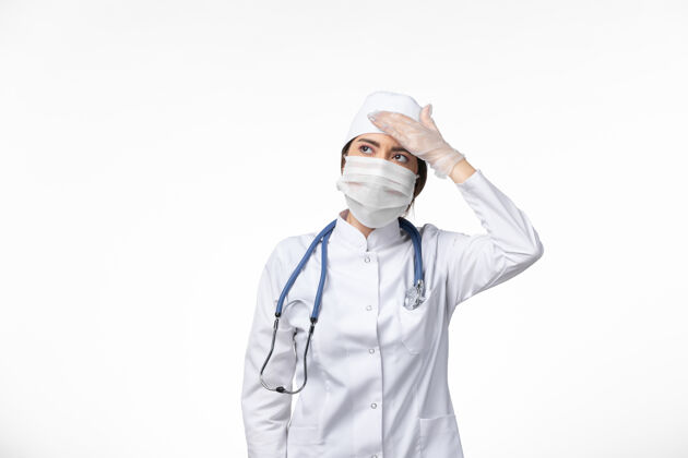听诊器正面图：女医生身穿白色无菌医疗服 戴口罩 因柯维德-头痛白墙病病毒柯维德-大流行性疾病医生人面罩