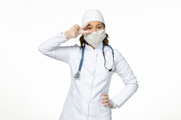 正面正面图女医生穿着白色医疗服 戴着口罩 因白墙上冠状病毒病大流行视图人员护士