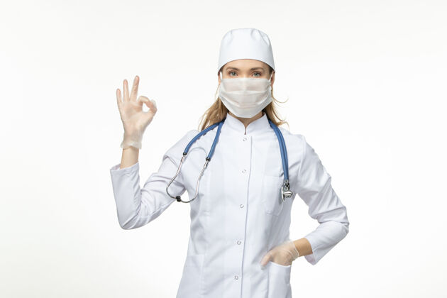 专业人员正面图女医生身穿医疗服戴口罩因白墙上冠状病毒病冠状病毒-大流行性疾病女性正面冠状病毒预防