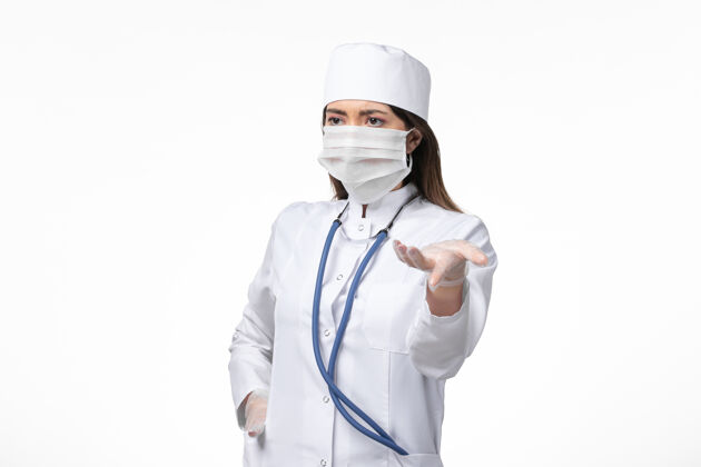 冠状病毒防护正面图女医生身穿白色无菌医疗服 带口罩 因白色办公桌上有冠状病毒-大流行性疾病病毒外套疾病听诊器